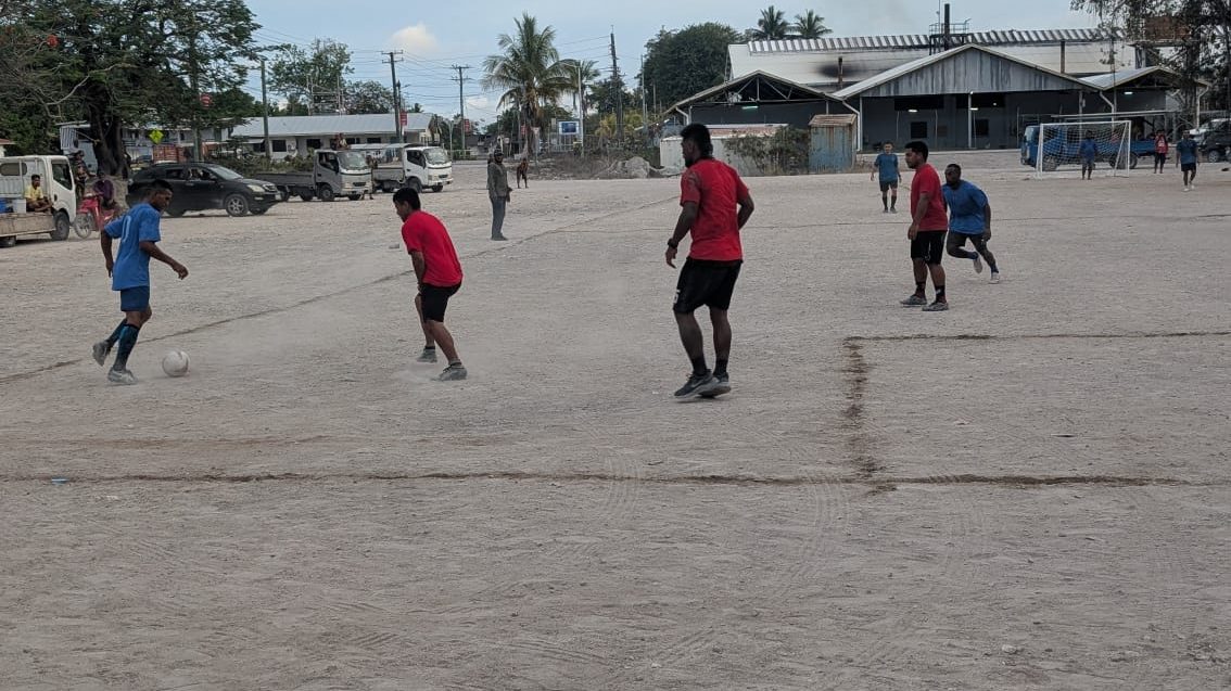 Children playing football on a sandy pitch on Naoero, with a goal and trees in the background